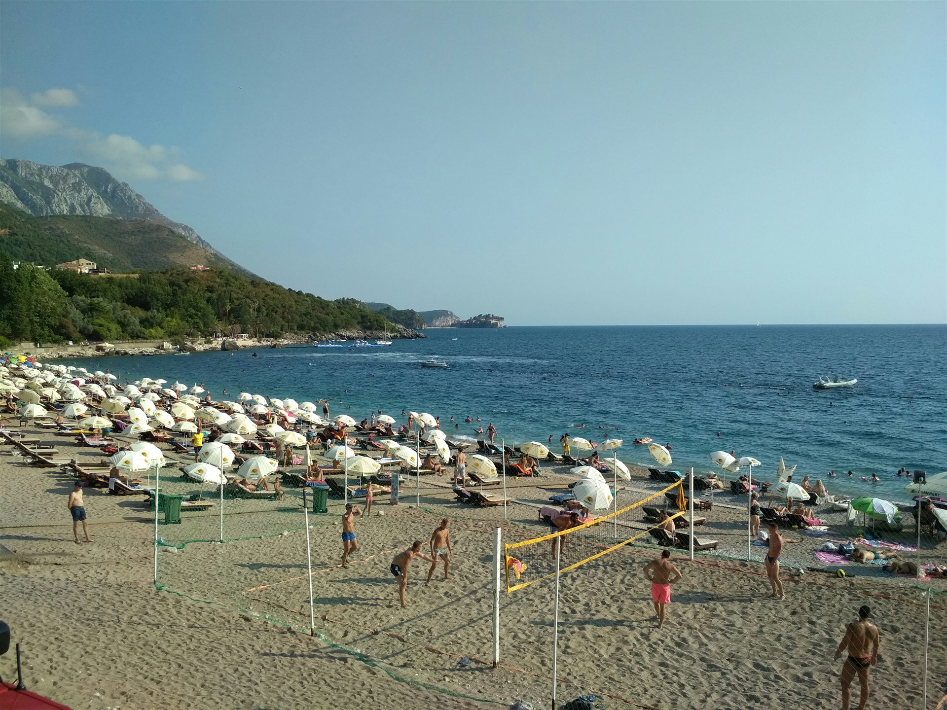 Beach volleyball players on a busy beach by the sea.