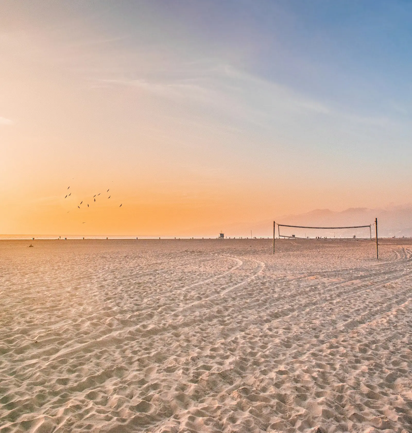 A beach volley court on the sand by the sea at sunset.
